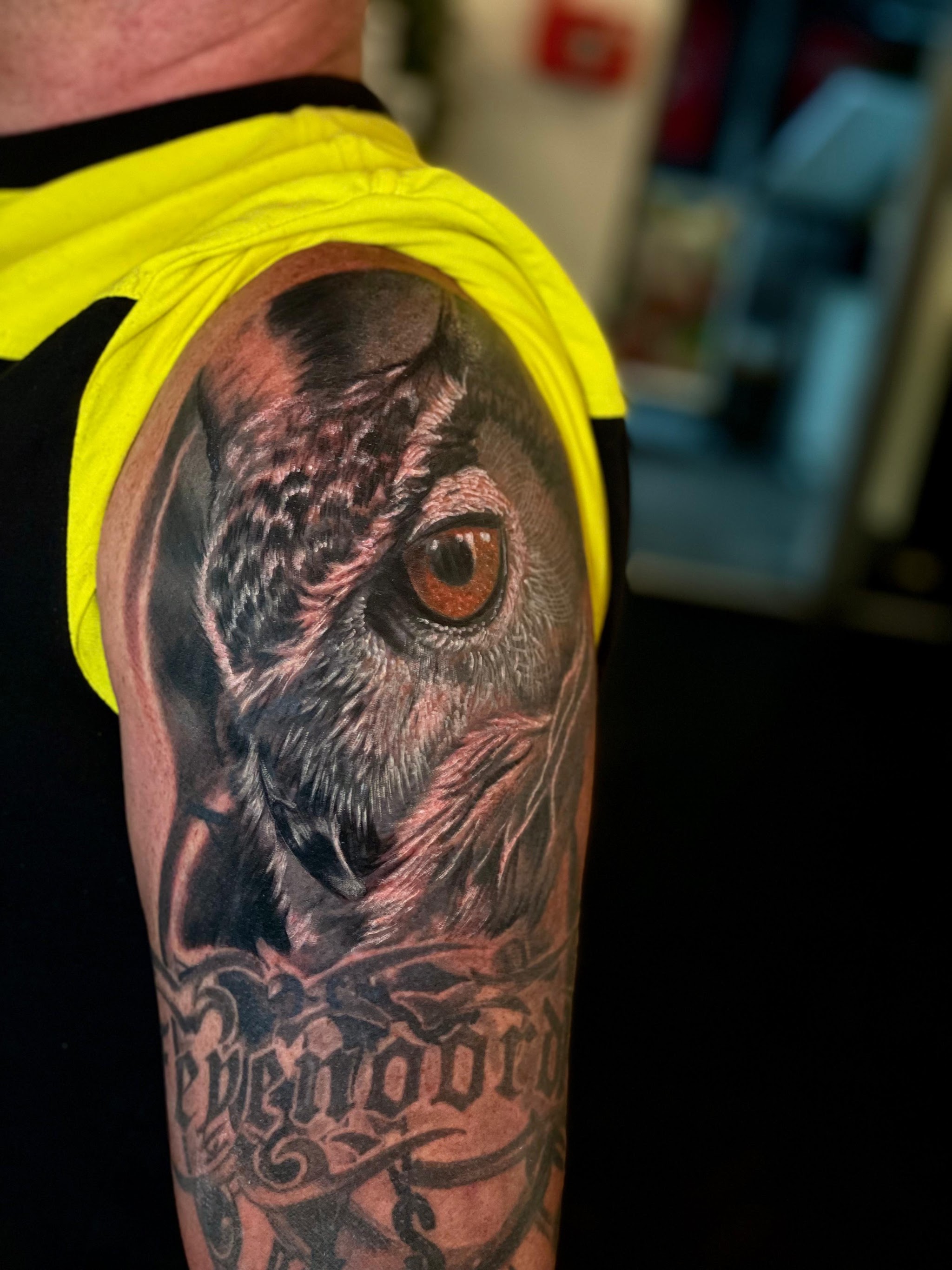 Realistische uil met oranje oog en lettering op de bovenarm
